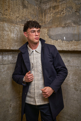 Man wearing glasses and a dark coat against a textured wall