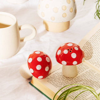 Red mushroom-shaped salt and pepper shakers with white spots on a book with a light background.