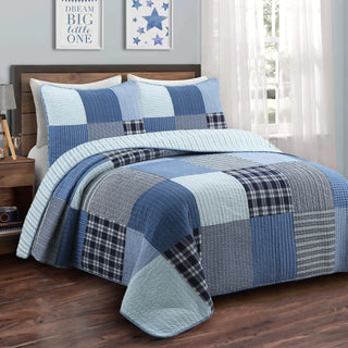 Blue patchwork quilt on a bed in a bedroom setting with decor elements.