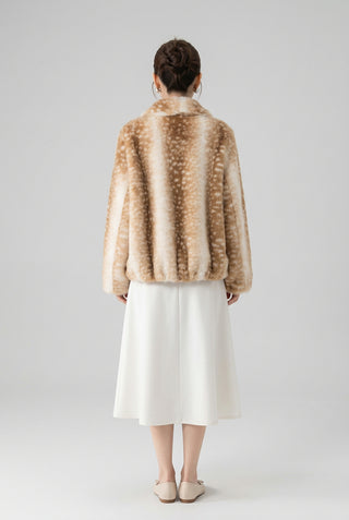 A woman shown from the back wearing a plush faux fur jacket with a brown and cream spotted pattern, paired with a gray pleated skirt, standing against a textured off-white wall.
