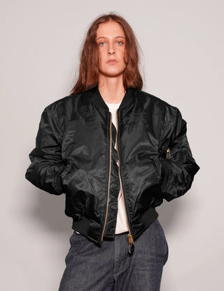 Person wearing a black bomber jacket on a plain background