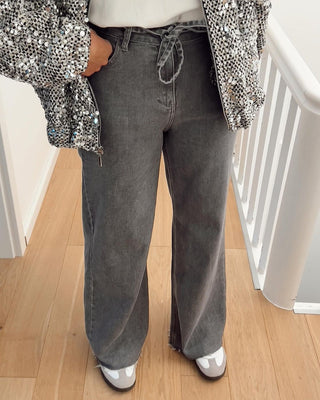 Person wearing gray wide-leg jeans and a patterned jacket on a wooden floor.