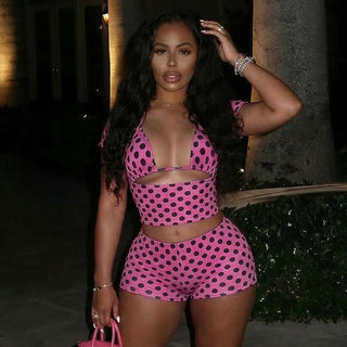 Woman wearing a pink polka dot outfit standing outdoors at night.