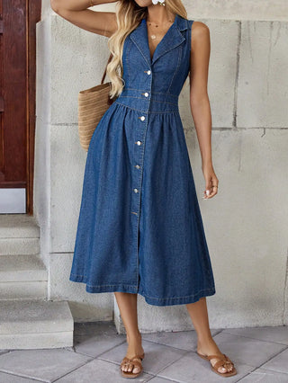 Woman wearing a blue denim dress standing against a stone wall.