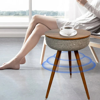 Round side table with wooden legs and gray top in a room with a person sitting on a chair.