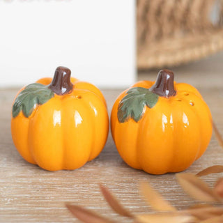 Two ceramic pumpkins with green leaves on a wooden surface.
