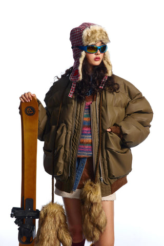 Person wearing winter clothing with a fur-lined hat and holding skis on a white background