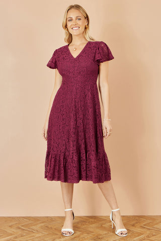 Woman wearing a burgundy lace dress against a beige background