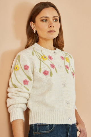 Woman wearing a cream sweater with floral embroidery against a beige background