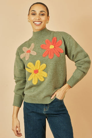 Woman wearing a green sweater with floral designs on a beige background