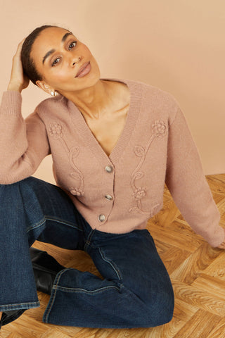 Woman wearing a pink cardigan with floral patterns sitting on a wooden floor.