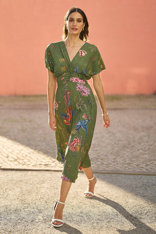 Woman wearing a green floral dress against a pink wall.