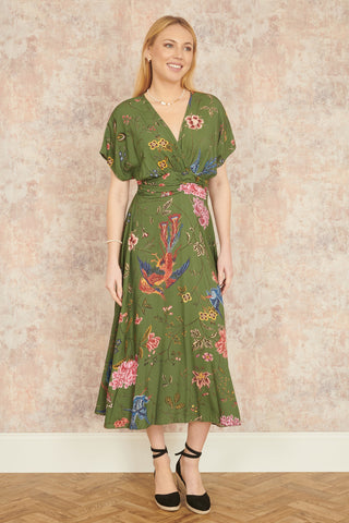 Woman wearing a green floral dress against a beige wall.