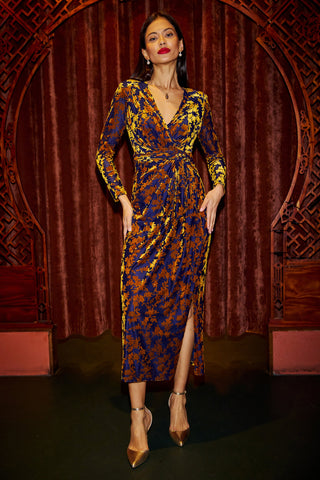 Woman wearing a patterned dress with a deep neckline and long sleeves against a decorative wall.
