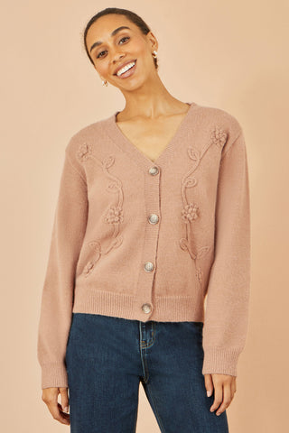 Woman wearing a pink cardigan with floral embellishments on a beige background