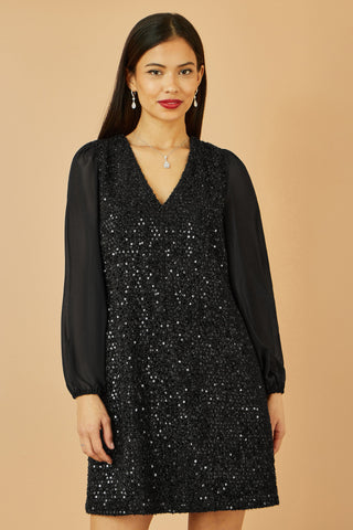 Woman wearing a black sequin dress against a beige background