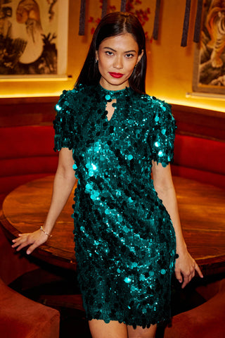 Woman wearing a green sequin dress in an indoor setting with red seats and framed pictures on the wall.