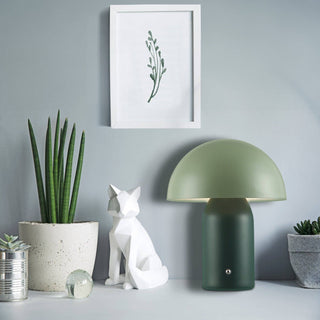 Green table lamp on a surface with decorative items against a gray wall.