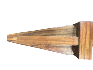 A close-up of a wooden object with a pointed triangular end and a rectangular block base, showing a warm brown wood grain on a dark textured surface.