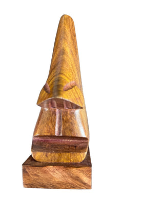 A hand-carved wooden sculpture of a stylized face with a long conical nose, mounted on a rectangular base, shown against a dark textured background.