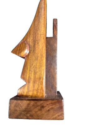 A small handcrafted wooden sculpture or decorative object with a warm medium-brown finish, photographed against a dark textured background.