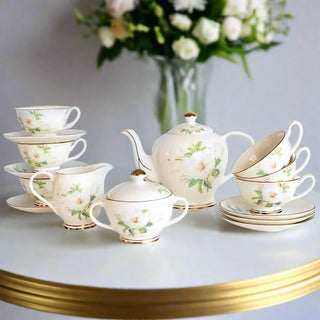 Tea set with floral designs on a table with a vase of flowers in the background