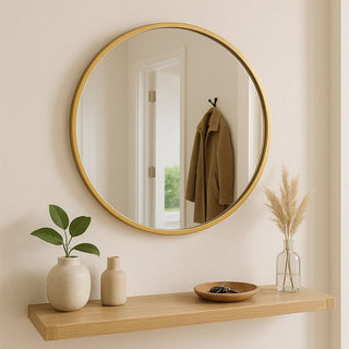 Round gold-framed mirror on a wall with a wooden shelf below containing decorative items.